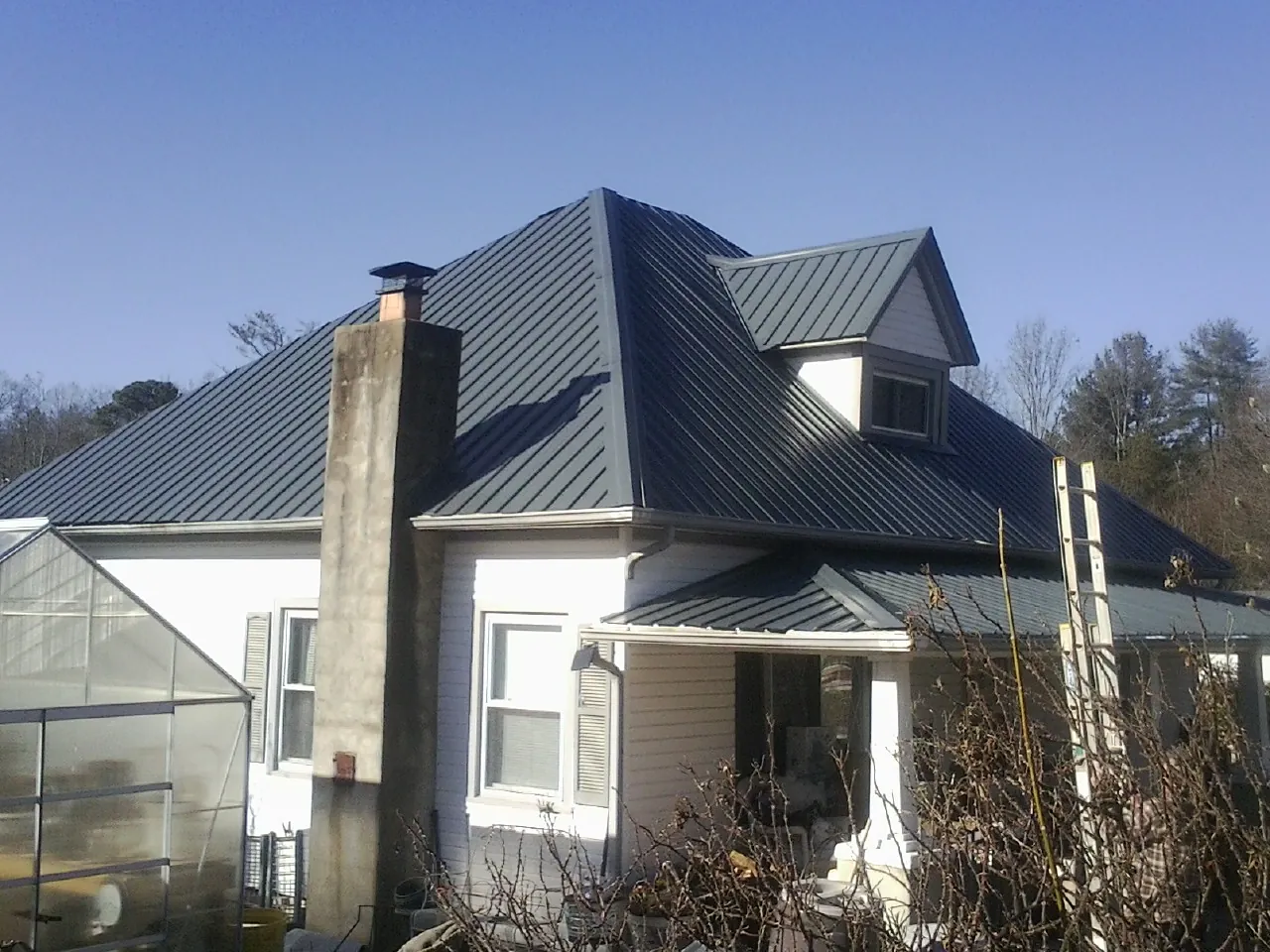 Dark blue standing seam metal roof on a white farmhouse with dormer — Slate & Tile Roof Repair by Roofing Brothers in Kesley