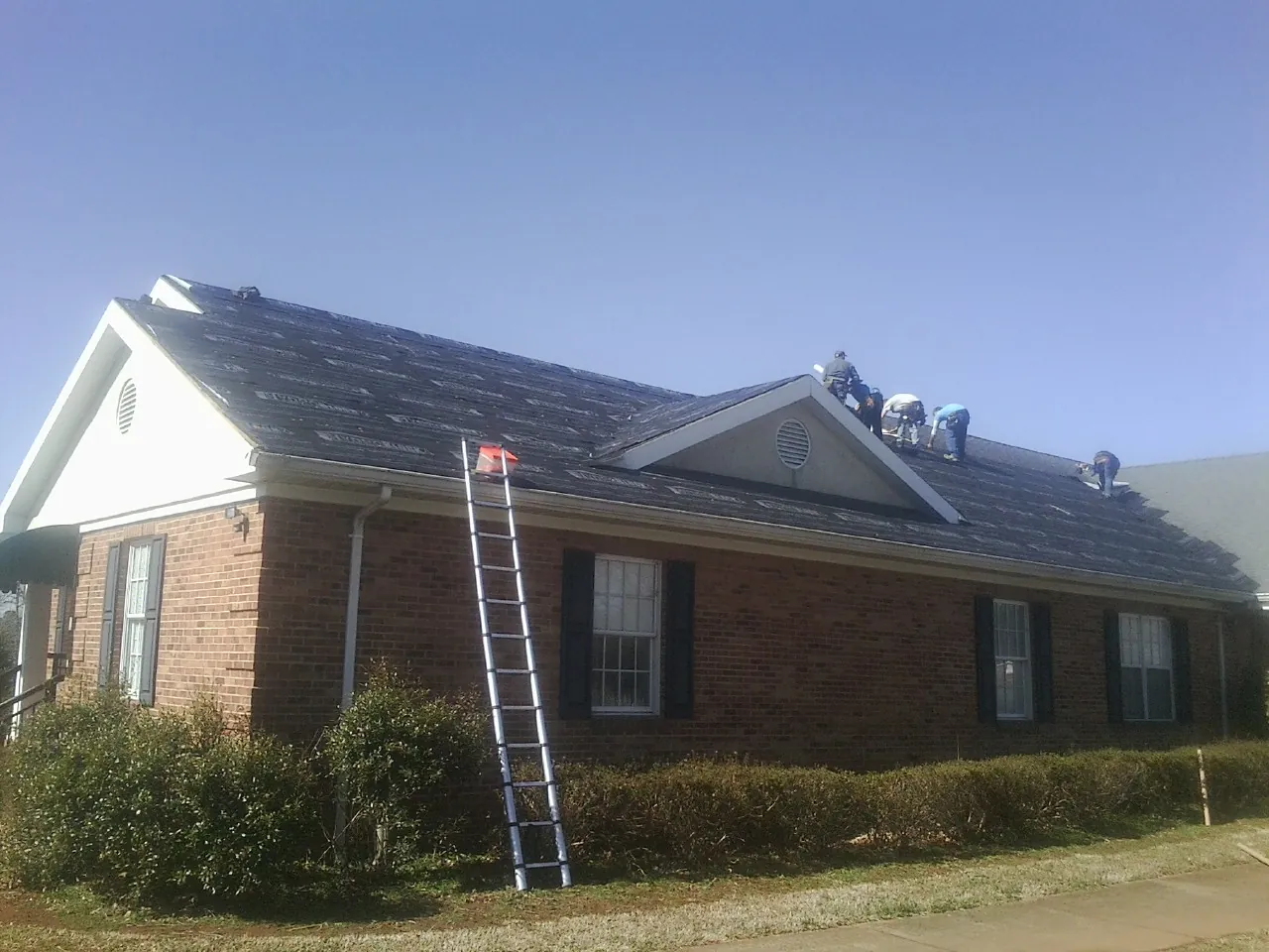 Crew tearing shingles off a brick ranch roof with a ladder set — Emergency Roof Repair work by our crew in Kesley