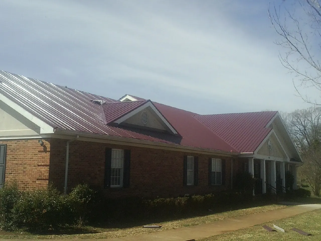 Red metal roof with gabled entries on a long brick building, from a Hail Damage Roof Repair job in Kesley