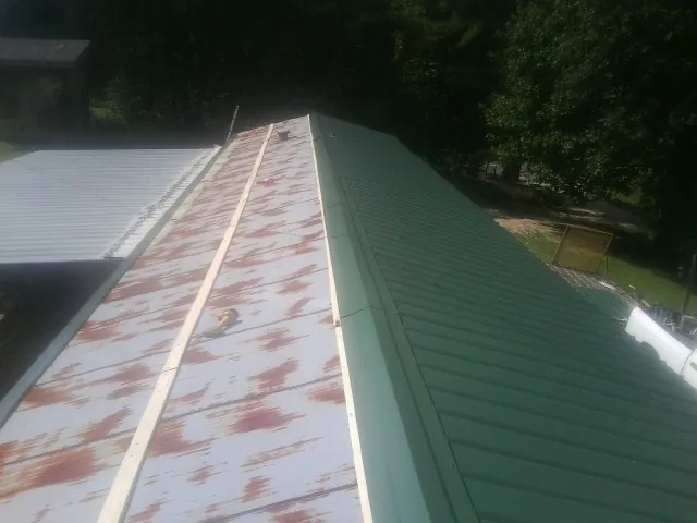Old rusted panels beside newly installed green metal roofing — Wind Damage Roof Repair by Roofing Brothers in Kesley