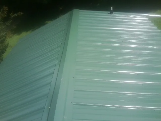 New green metal panels meeting at the ridge of a roof — Flat Roof Repair work by our crew in Kesley