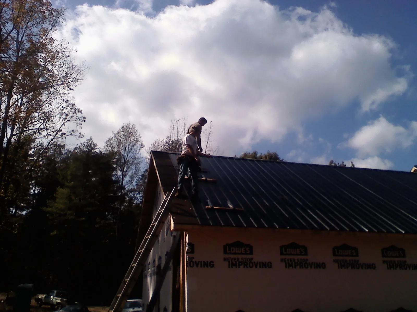 Roofer fastening dark metal panels high against a cloudy sky, from a Roof Inspection job in Kesley