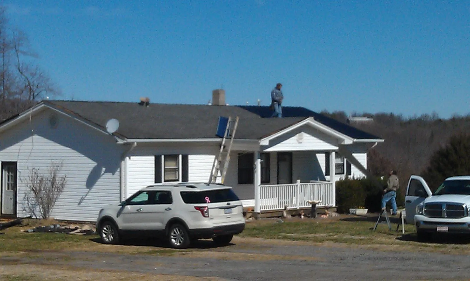 Roofers stripping shingles from a white ranch house roof in Kesley