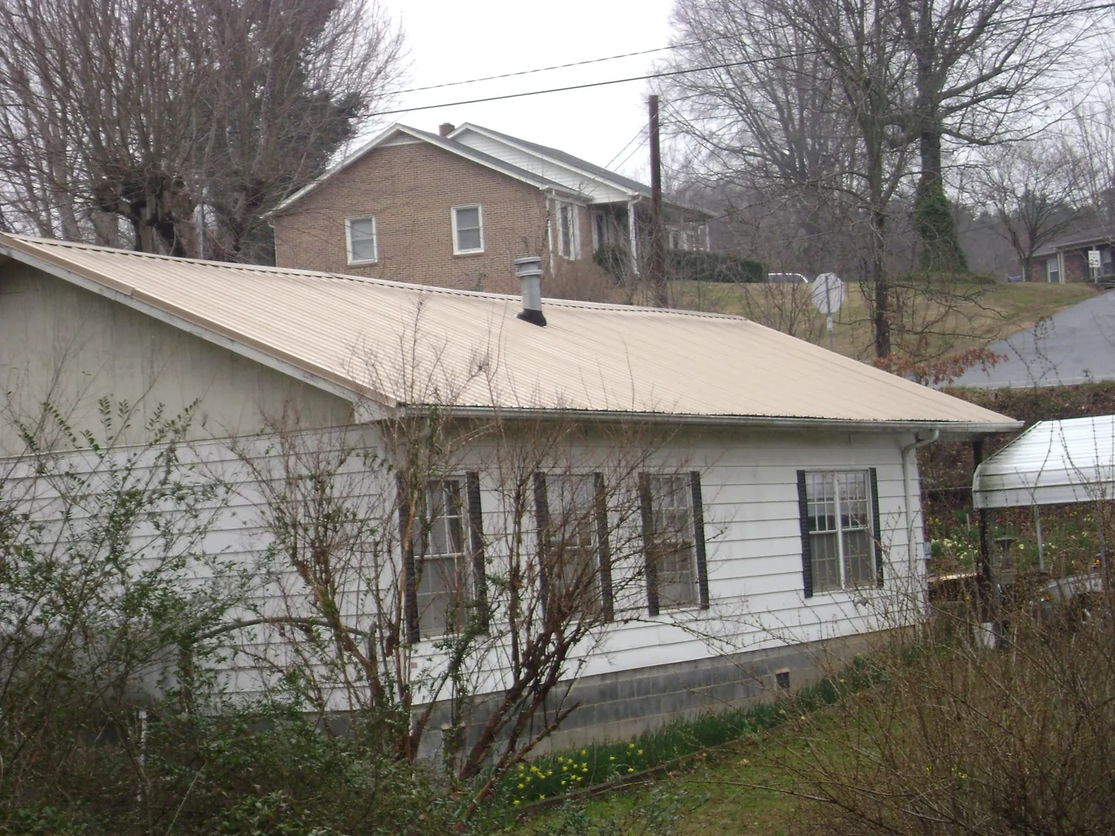 Tan metal roof on a white sided house set into a hillside — Commercial Roofing by Roofing Brothers in Kesley