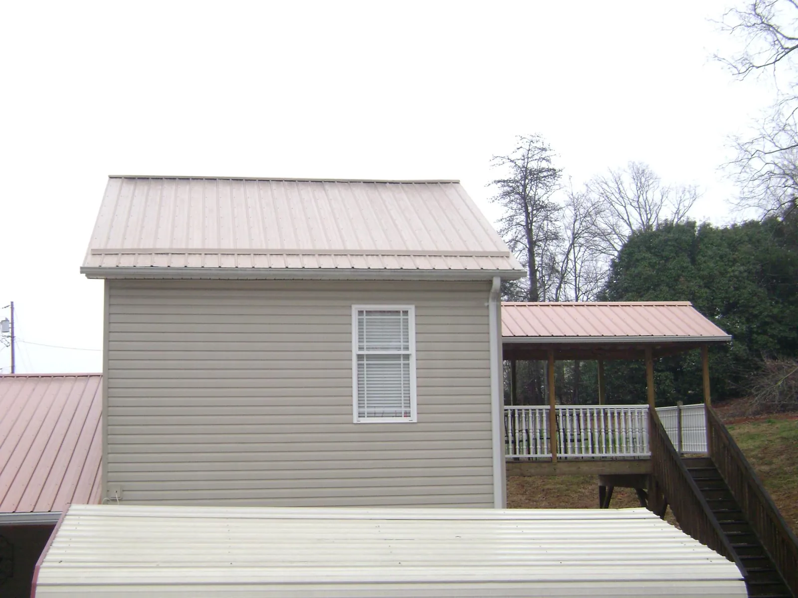 Tan metal roofs on a two story addition and attached porch, from a Roof Replacement job in Kesley